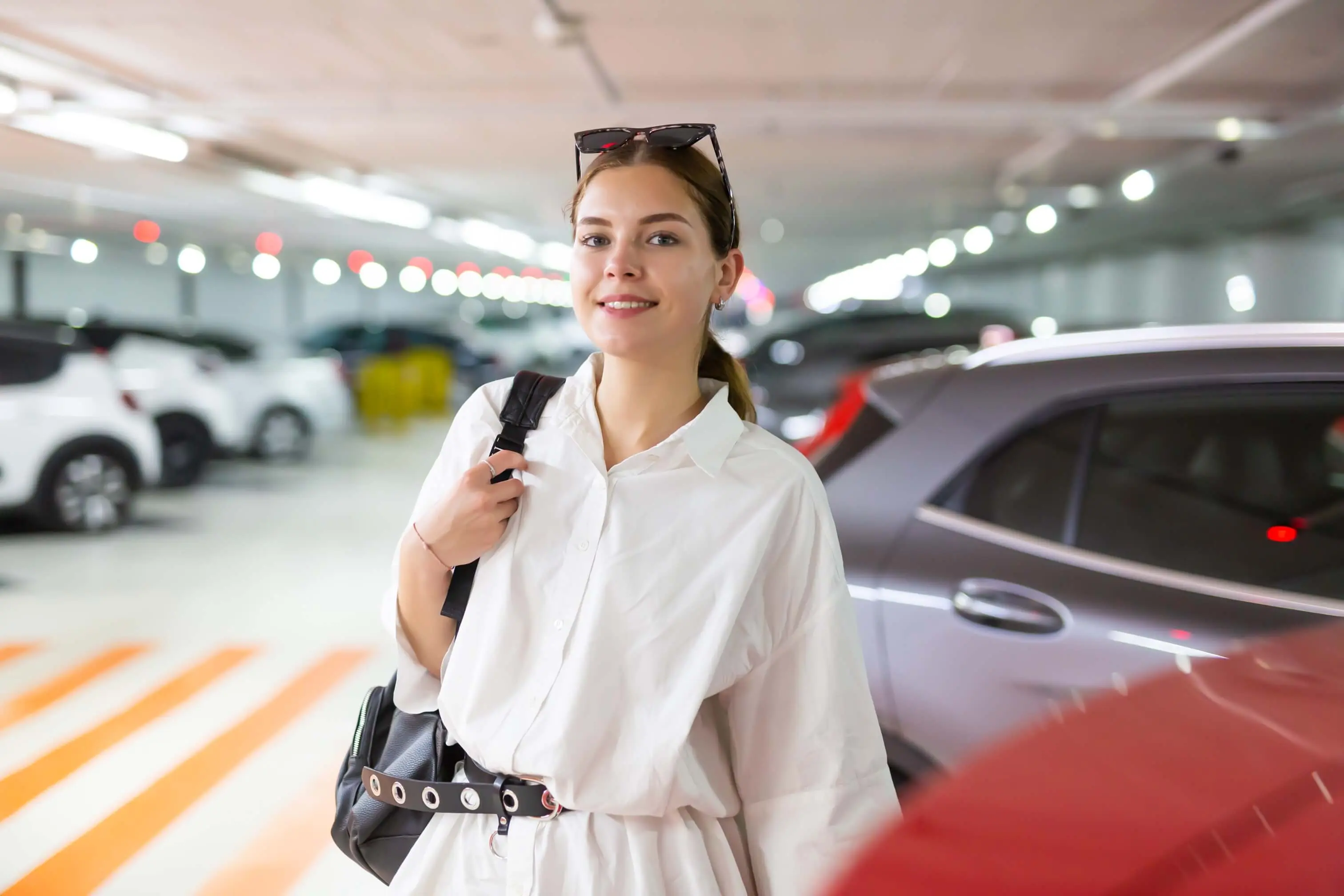 Mulher sorridente chegando em estacionamento coberto, simbolizando praticidade e conforto do plano estapar mensal.
